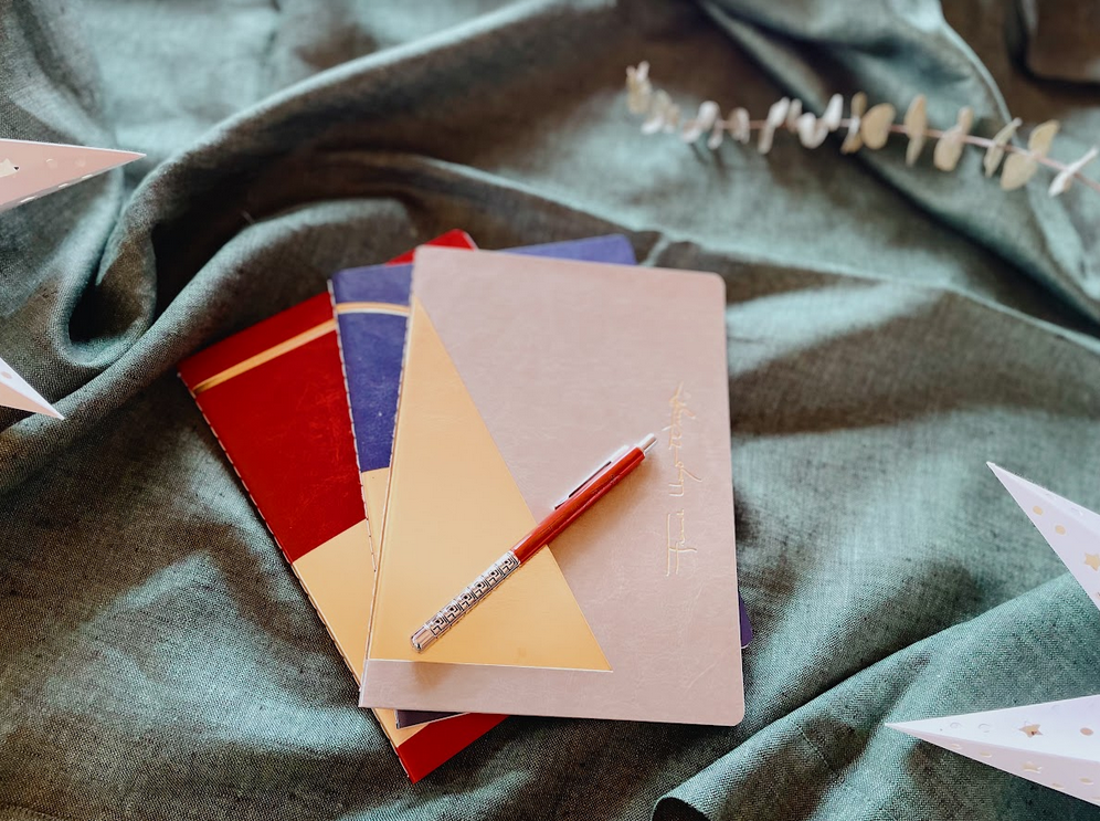 Set of three notebooks in red, blue and gold pictured with a red mechanical drafting pencil. Recommended in the 2021 Gift Guide.